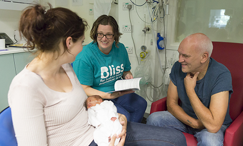 Volunteer chatting and smiling with parents with mum holding baby in a unit